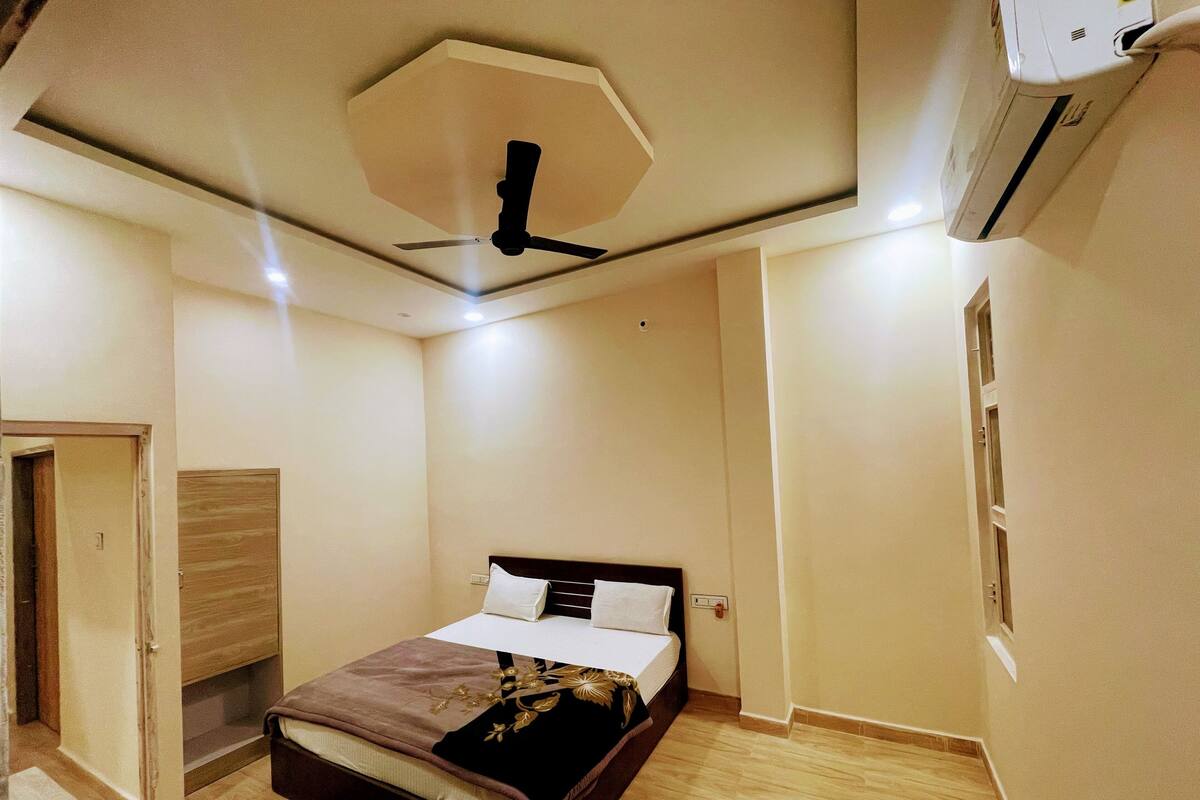Ein Schlafzimmer mit einem Bett, einem Deckenventilator, einer Klimaanlage und einer Holztür.