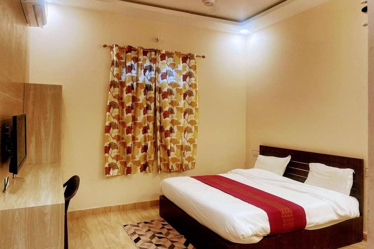 Ein Schlafzimmer mit Bett, Vorhängen, Fernseher und Stuhl.