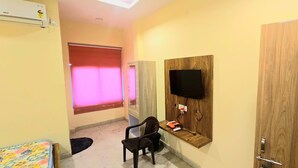 A hotel room with a wooden door marked "108", a TV mounted on a wooden panel, a chair, a small table with items, and a window with pink lighting. - Sunrise Hotel & Restaurant (Danta Ramgarh)