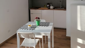 A modern kitchen with white cabinets, a microwave, and a sink. There is a dining table with a black and white striped tablecloth and a green potted plant. - Dell'Ova 98 Rooms (Catania)