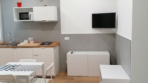 A modern kitchen with white cabinetry, a microwave, a gas stove, and a flat-screen TV mounted on the wall. - Dell'Ova 98 Rooms (Catania)