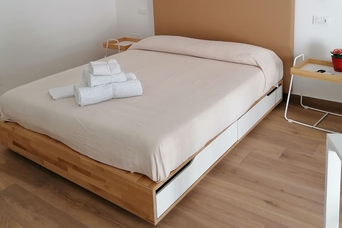 A neatly made bed with a wooden frame, a bedside table with a tray, and a small potted plant.
