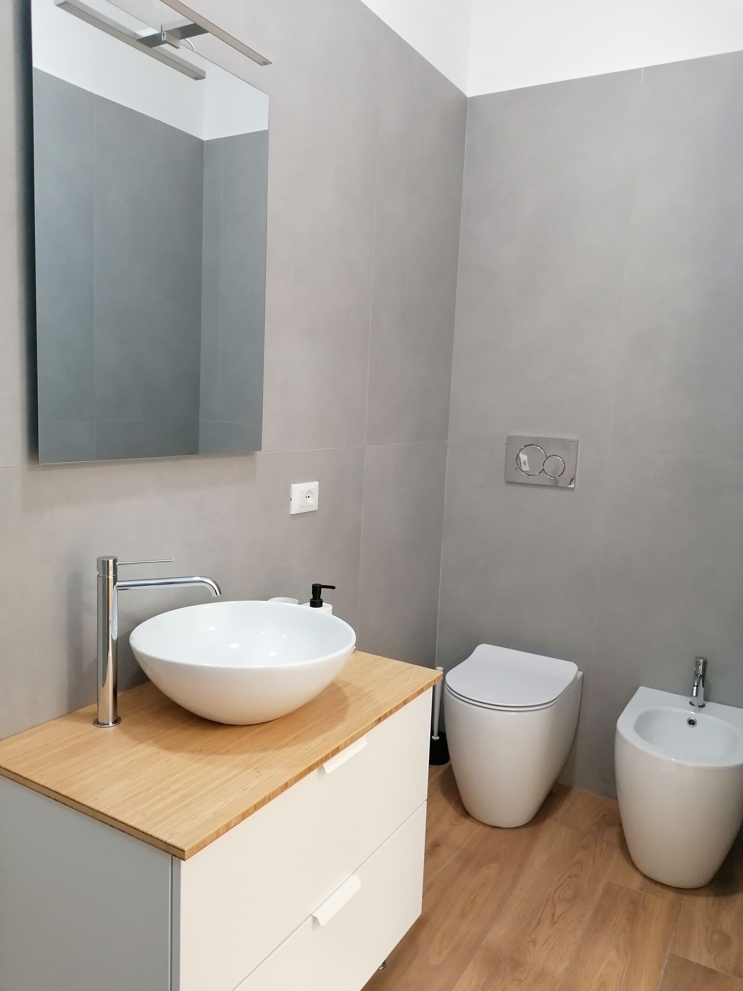 A modern bathroom with a large mirror, a white sink with a wooden countertop, a bidet, and a toilet.
