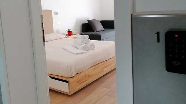 A modern hotel room with a wooden floor, a bed with white linens, a black headboard, and a red cup on the nightstand. - Dell'Ova 98 Rooms (Catania)