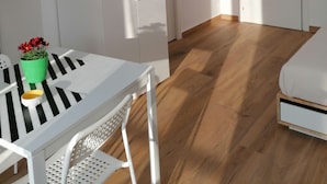 A modern, minimalist room with a white table, a green vase with flowers, a white chair, a flat-screen TV mounted on the wall, and a wardrobe. - Dell'Ova 98 Rooms (Catania)