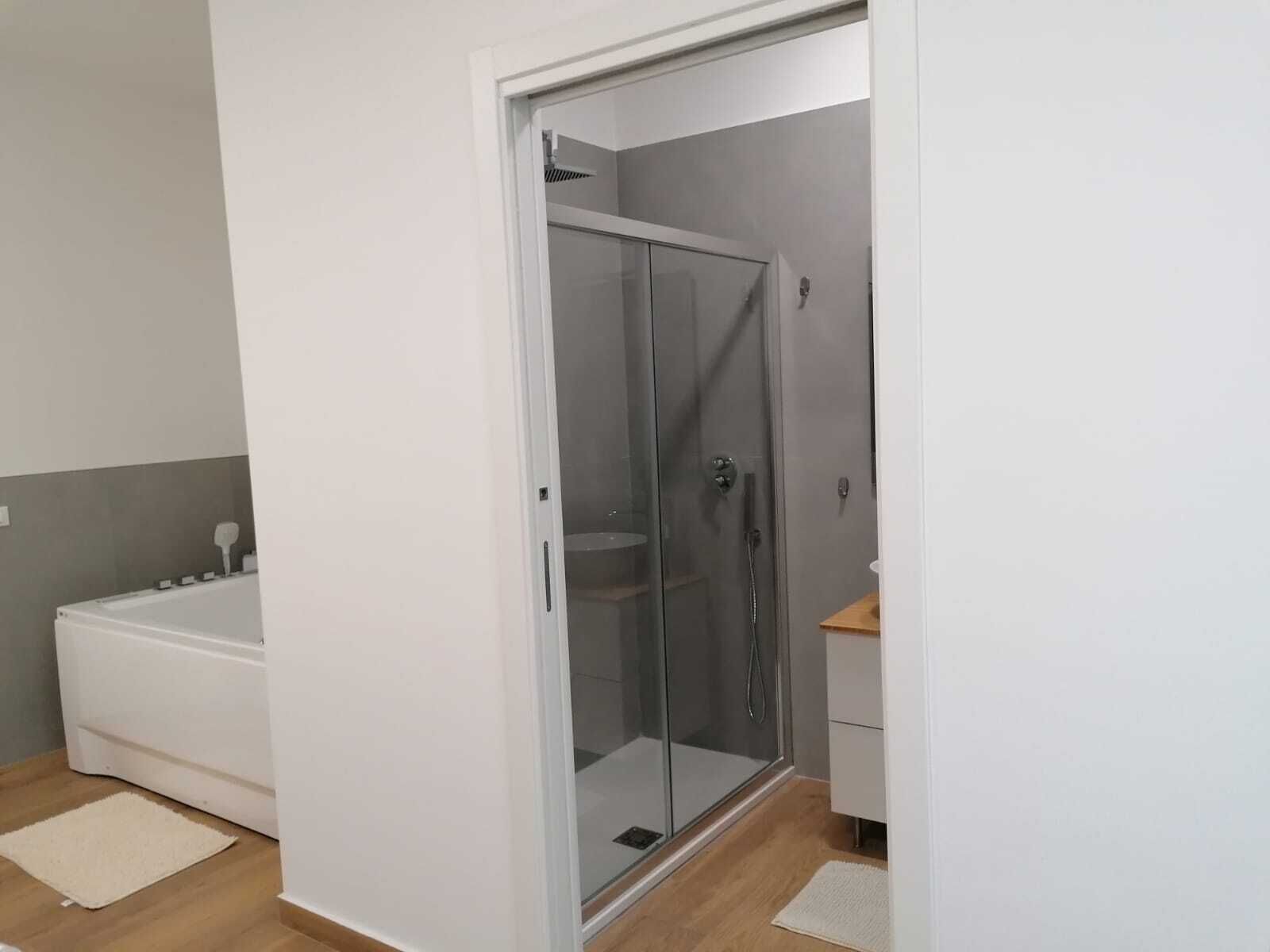 A modern bathroom with a glass shower enclosure, a white bathtub, and a wooden vanity.