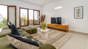 A modern living room with a sectional sofa, a TV, a wooden console, and a patterned rug. - Canggu Garden House (Canggu)