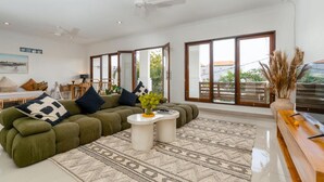 A modern living room with a green sofa, a coffee table, and a large window with a view of the outdoors. - Canggu Garden House (Canggu)