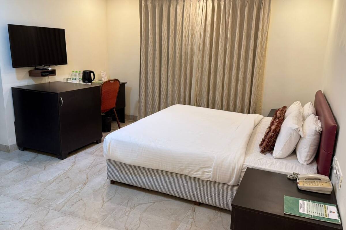 A hotel room with a bed, a desk with a television, a telephone, and a small table with a menu.