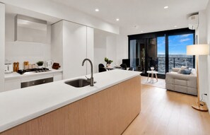 A modern kitchen with a central island, a dining area with a view, and a living space with a sofa and lamp.