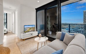 A modern living room with a flat-screen TV, a sofa, and a balcony with a city view.