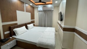 A hotel room with a large bed, a ceiling fan, an air conditioning unit, a television, and a bedside table with a phone and charger. - Hotel Nandan Inn (Gaya)