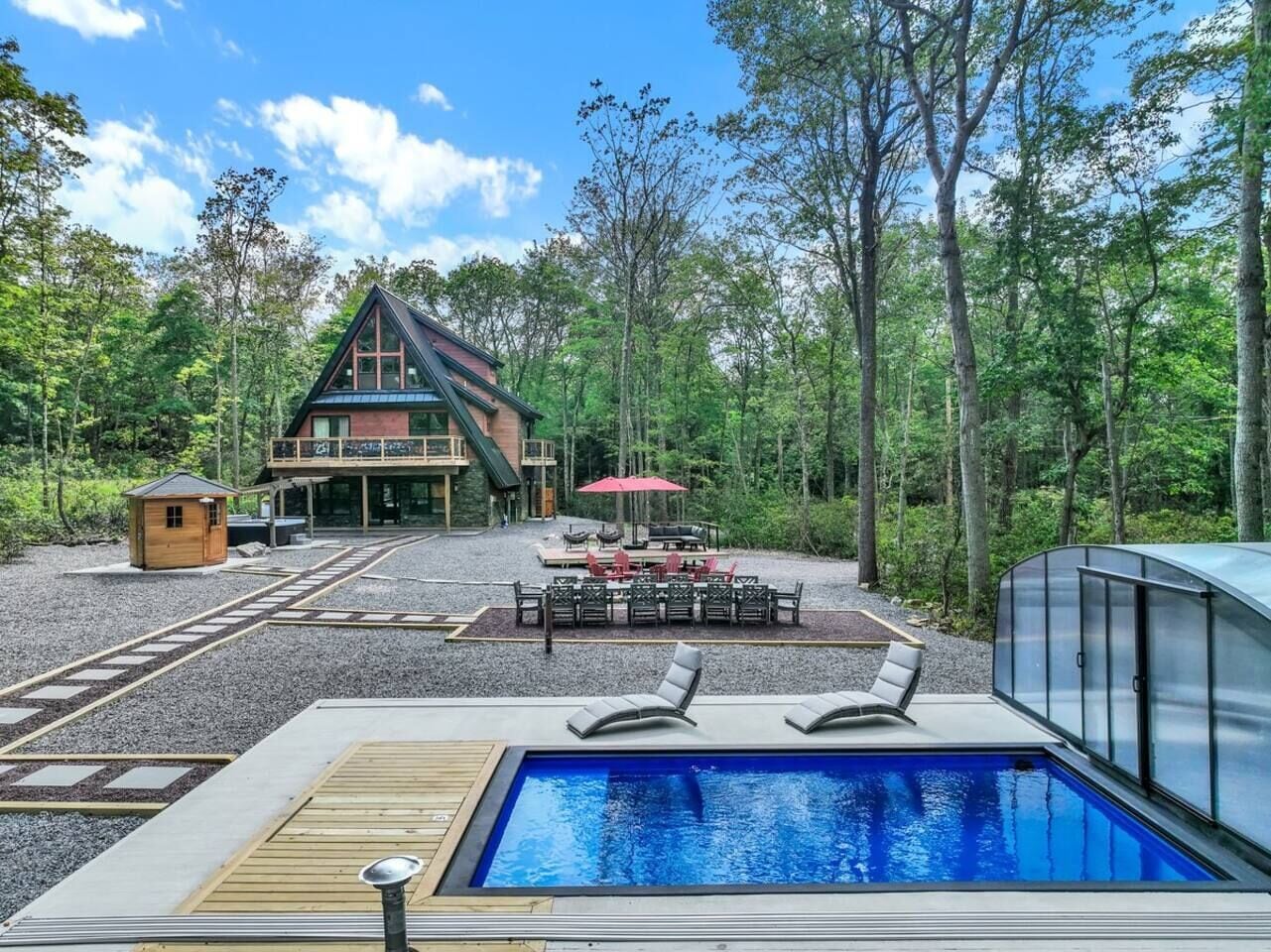 Un área de piscina con sillones de descanso, una pequeña estructura de madera y un comedor con mobiliario exterior.
