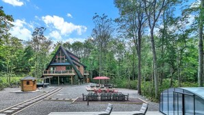 A pool area with lounge chairs, a small wooden structure, and a dining area with outdoor furniture. - Bliss A-Frame, Heated Pool AxeThrow Sundeck Sauna HotTub FirePit (Jim Thorpe)