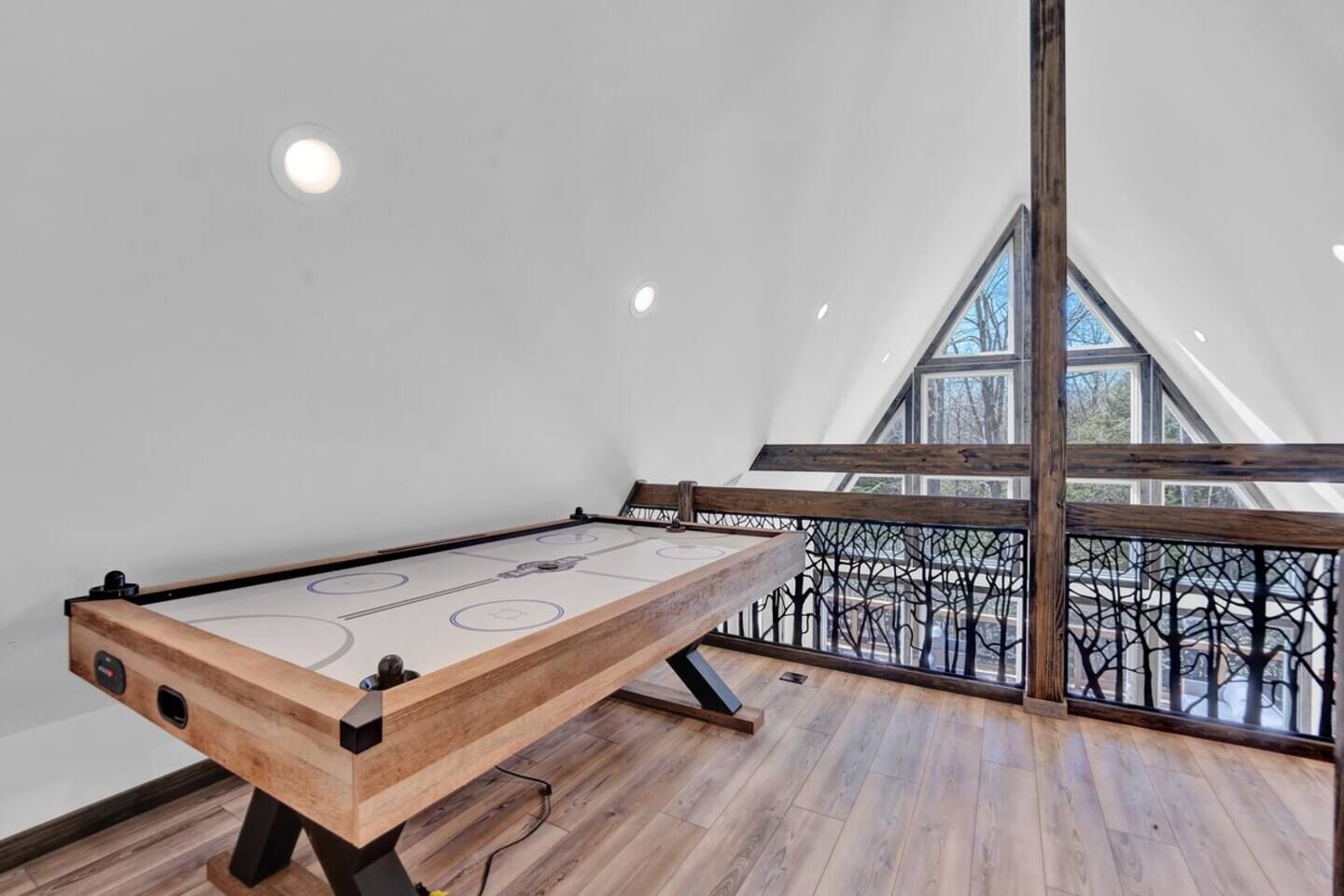 Una stanza con tavolo da shuffleboard in legno, un balcone con ringhiera in ferro battuto e un soffitto alto con lucernari.