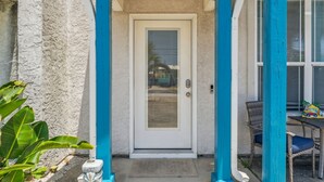 Una casa con puerta blanca, columnas azules y un porche con muebles de mimbre.