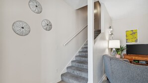 Una escalera con barandilla, un sillón tapizado gris, un televisor de pantalla plana y adornos en la pared.