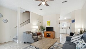 Una sala de estar con sofá, una mesa de centro y un mueble para televisión. Se ve una escalera que sube a otro nivel.