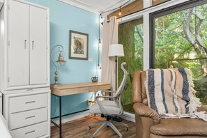 A room with a desk, chair, and a large window with a view of trees. - Zen Studio at Lotus Garden Cafe (Panama City Beach)