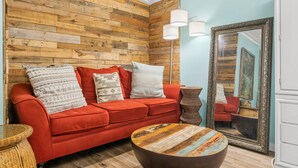 Una habitación con un sofá rojo, almohadas estampadas, una mesa redonda de centro, un espejo grande y una pared de madera.