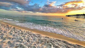 A beach with a pier extending into the ocean, waves gently lapping at the shore, and a clear sky above. - Sterling Breeze (Panama City Beach)