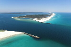 Ett flygbildsbild av ett kustområde med en sandstrand, klart blått vatten och en liten ö med tät vegetation.