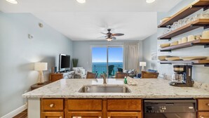 A kitchen with a marble countertop, wooden cabinets, a dishwasher, and a view to the ocean. - Sterling Breeze (Panama City Beach)
