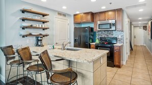 A modern kitchen with wooden cabinets, stainless steel appliances, and a bar area with stools. - Sterling Breeze (Panama City Beach)