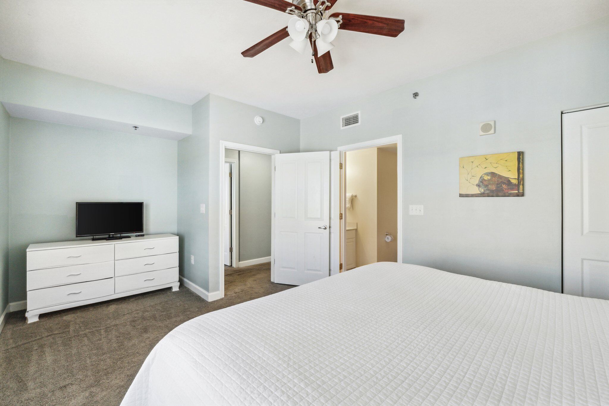 A bedroom with a bed, a dresser, a ceiling fan, and a television.