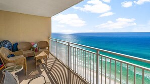 A balcony with wicker furniture, a glass table, and a view of the ocean. - Emerald Beach Resort (Panama City Beach)