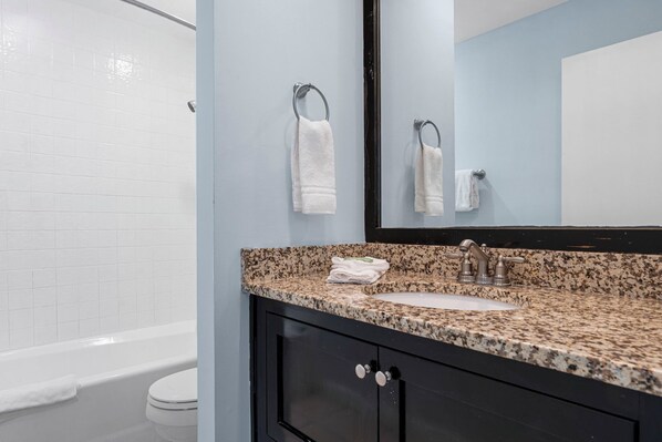 A bathroom with a granite countertop, a sink, a mirror, and a toilet. - Seahaven Penthouse (Panama City Beach)