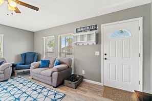 A living room with a grey wall, a white door, and a ceiling fan.