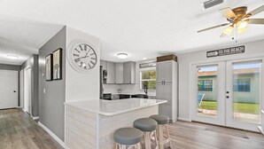 A modern kitchen with a central island, bar stools, a clock, and a sign indicating a beach direction. - Sunny Daze Cottage (Panama City Beach)