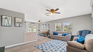 A spacious living room with a large sofa, a dining area, and a ceiling fan. - Sunny Daze Cottage (Panama City Beach)