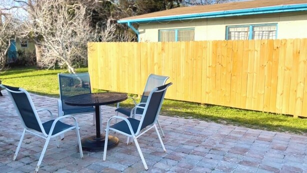 A patio with a round table and two chairs, a wooden fence, and a house in the background. - Sunny Daze Cottage (Panama City Beach)