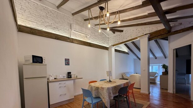 Un comedor con una mesa de madera, sillas y una cocina equipada con refrigerador y microondas.