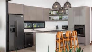 Une cuisine moderne dotée d’un îlot central intégré, d’appareils électroménagers en acier inoxydable et de luminaires suspendus.