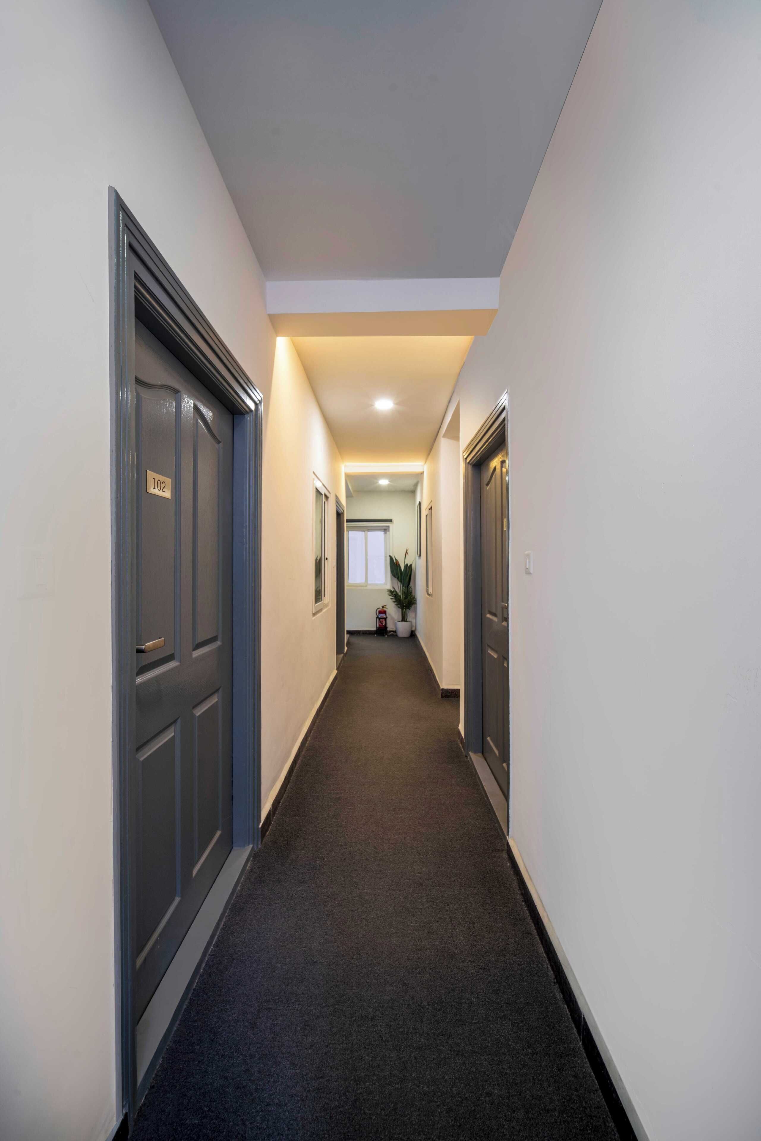 A narrow, carpeted hallway with closed doors on both sides, leading to a brightly lit room at the end.