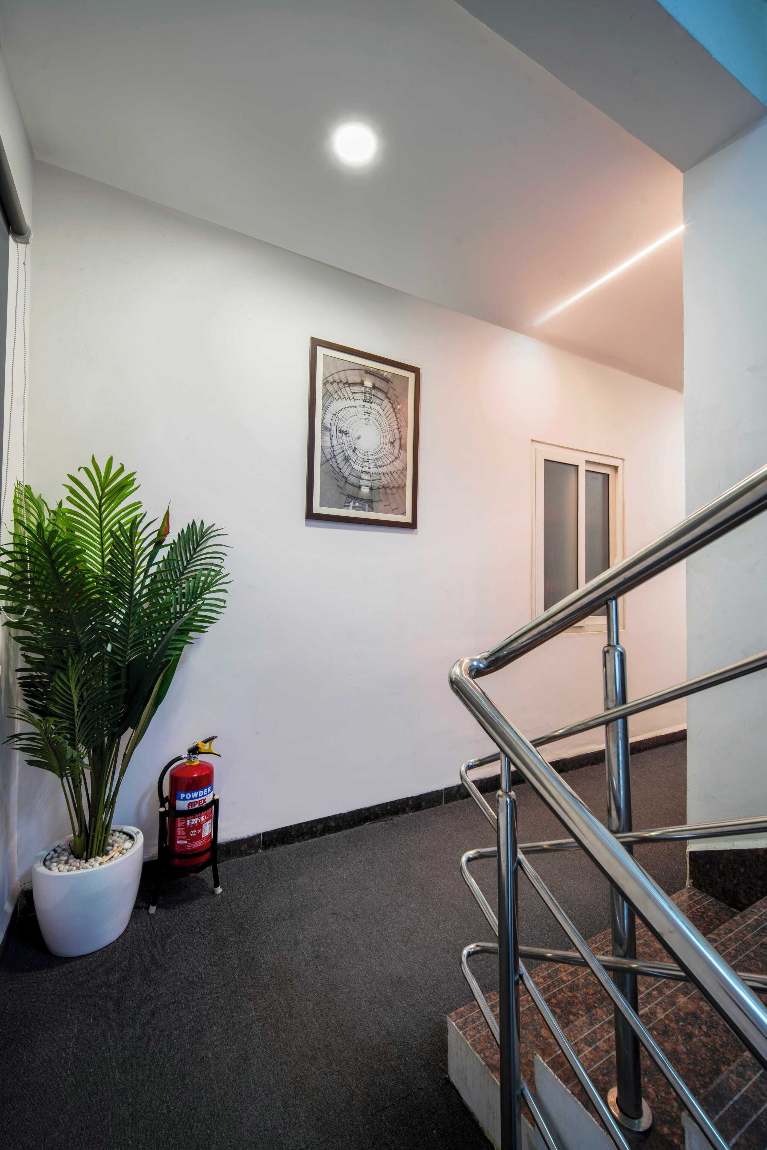 A hallway with a staircase, a framed artwork on the wall, a potted plant, and a fire extinguisher.
