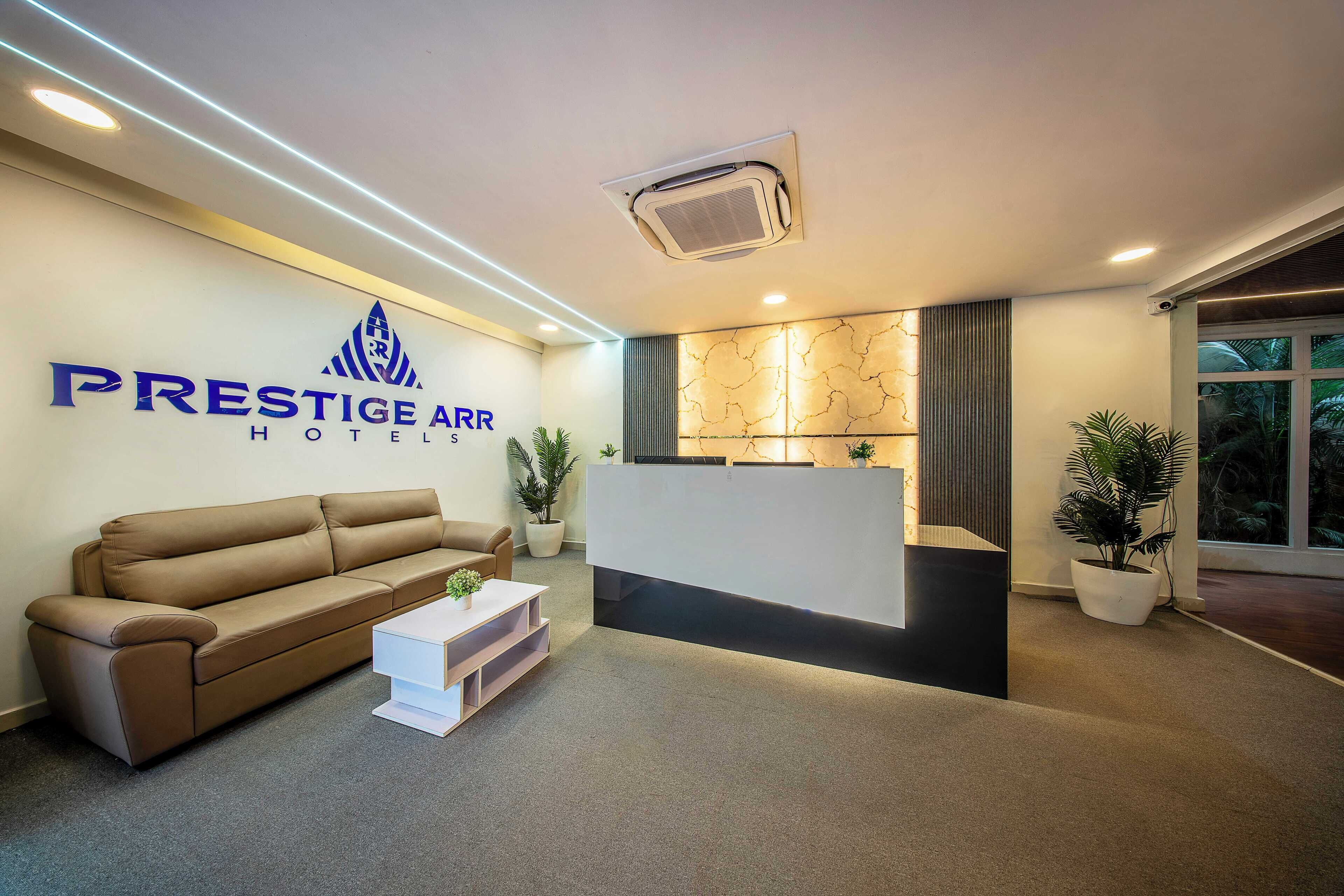 A hotel reception area with a brown sofa, a white reception desk, and a potted plant.