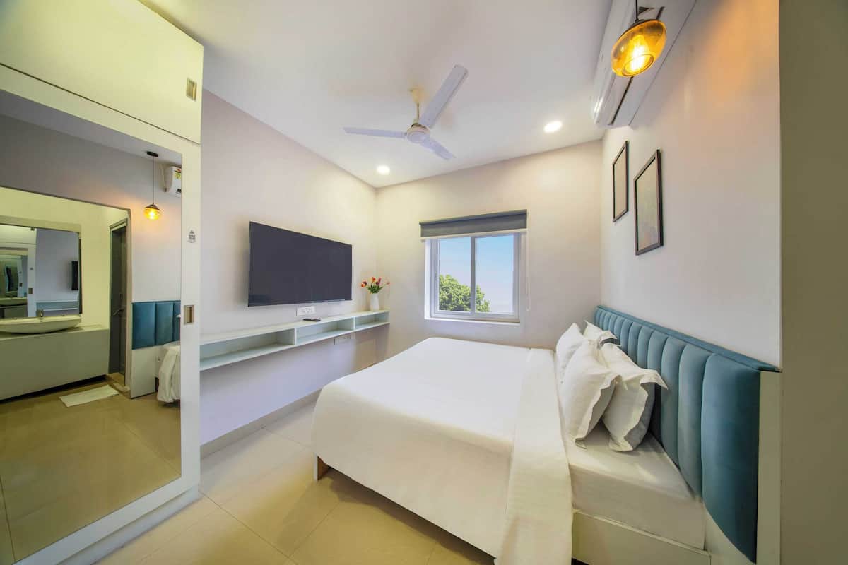 A modern bedroom with a bed, a TV, a window, and a ceiling fan.