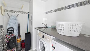 Ett utrymme för tvätt med en tvättmaskin, ett torkställ, en korg och en mopp.