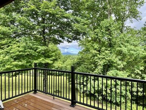 A wooden deck with a black railing overlooking a lush green landscape with trees and a distant mountain. - Dale Hollow Cabin · 3 Levels · Hot Tub · Huge Fire Ring · Sleeps 10 (Jamestown)