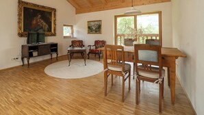 Ein geräumiges Wohnzimmer mit Holzböden, einem Essbereich mit Holztischen und -stühlen sowie einem großen Fenster mit Blick auf Bäume.