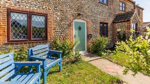 Una casa de piedra con puerta verde, un banco azul y un pequeño jardín.
