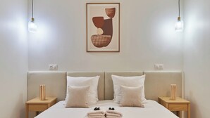 Una cama bien hecha con una toalla doblada, dos mesitas de noche con lámparas y una obra de arte abstracto enmarcada en la pared.