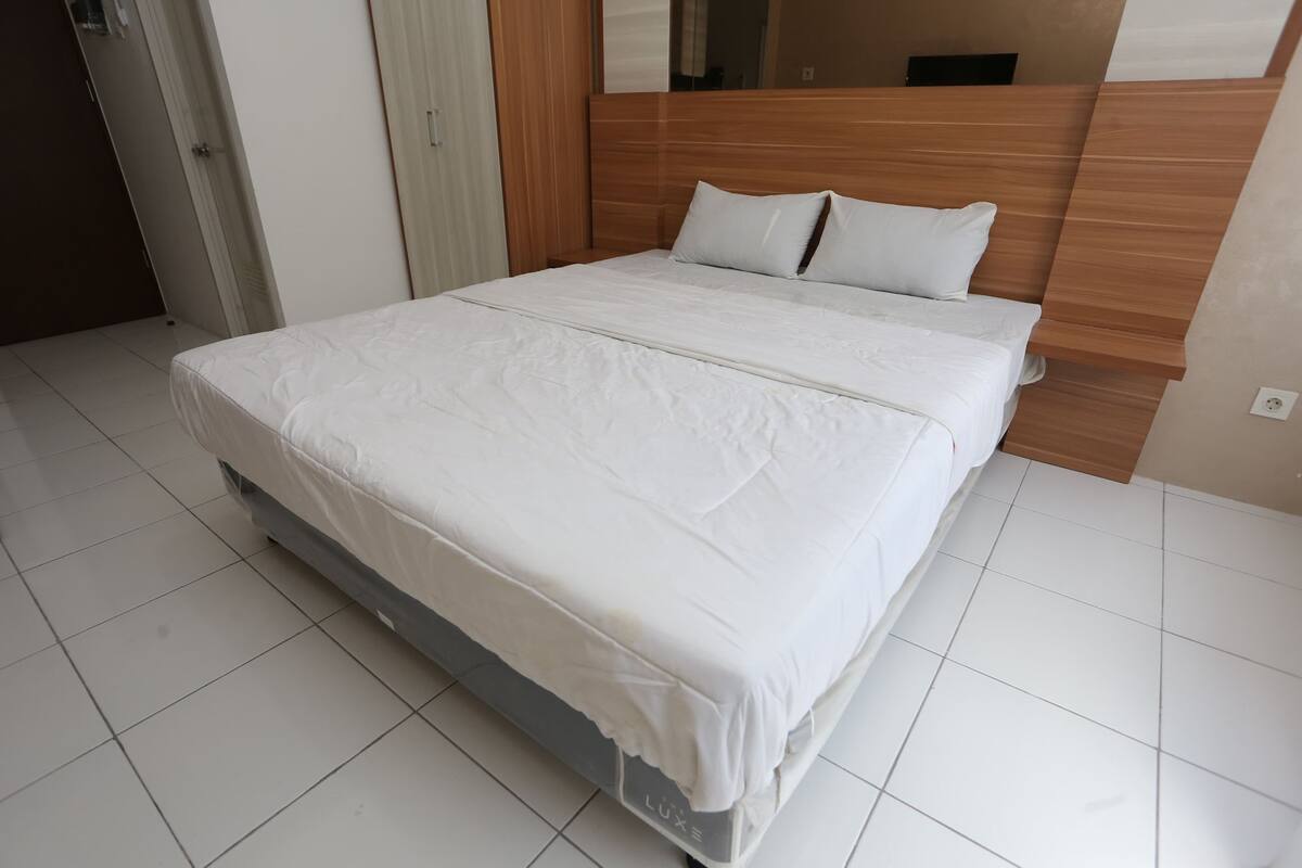 A neatly made bed in a hotel room with a wooden headboard and white bedding.