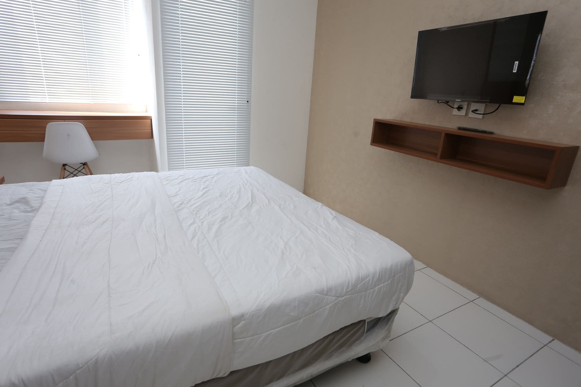 A bedroom with a bed, a TV mounted on the wall, and a small wooden shelf.