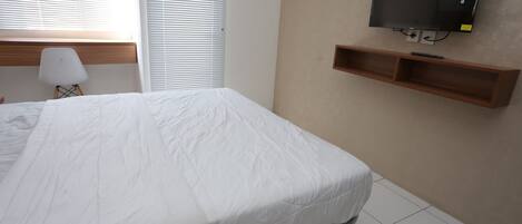 A bedroom with a bed, a TV mounted on the wall, and a small wooden shelf.