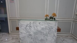 A reception desk with a marble top, two small flower arrangements, and a "No Smoking" sign on the wall. - Capital O Iconic Rooms @ Golden City (Bekasi)